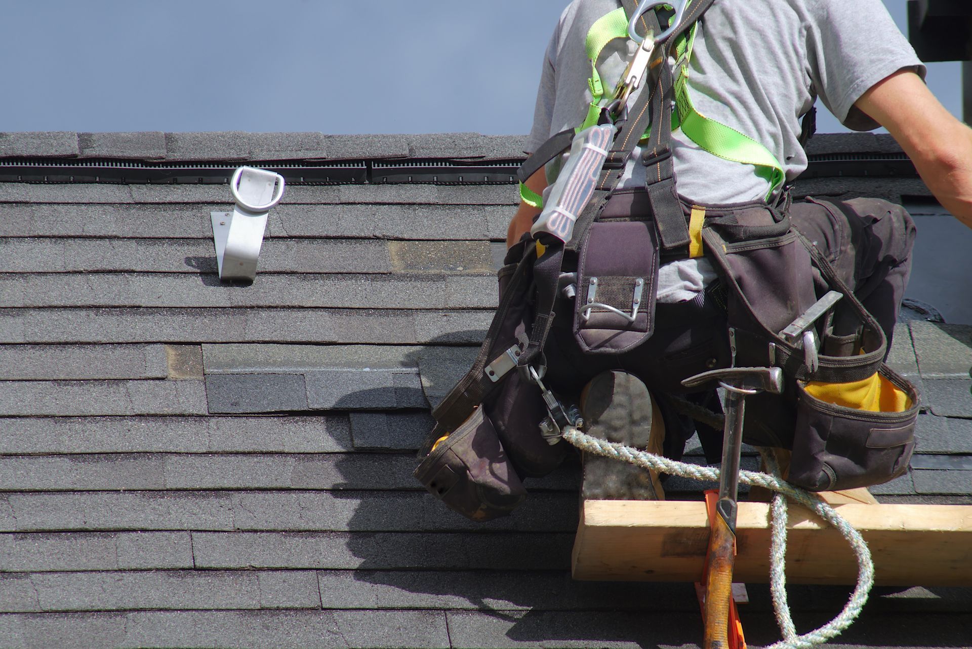 Worker with safety harness on a roof, carrying tools while repairing shingles.
