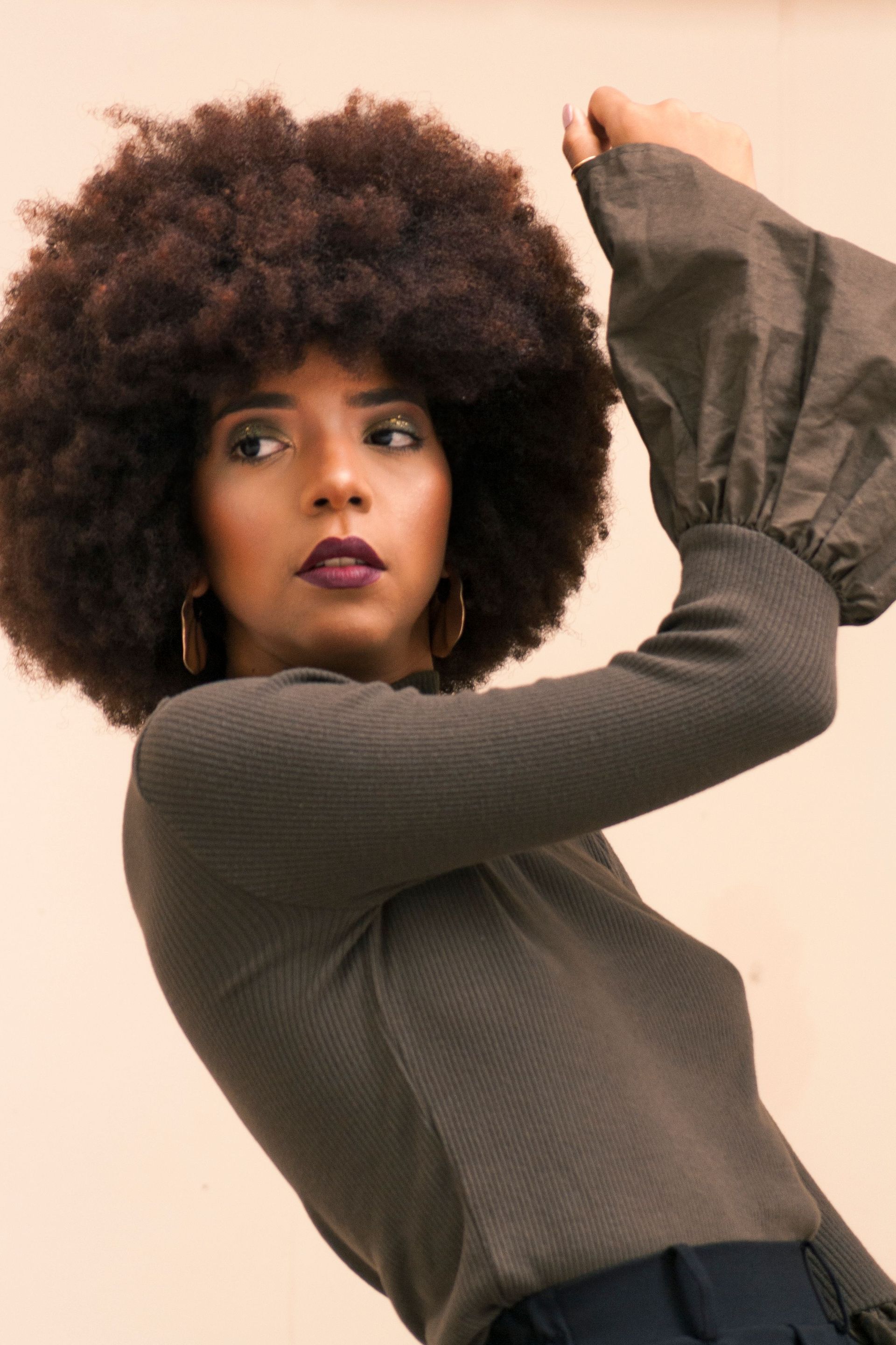 Woman with an afro posing in a dark top, arm raised against a light background