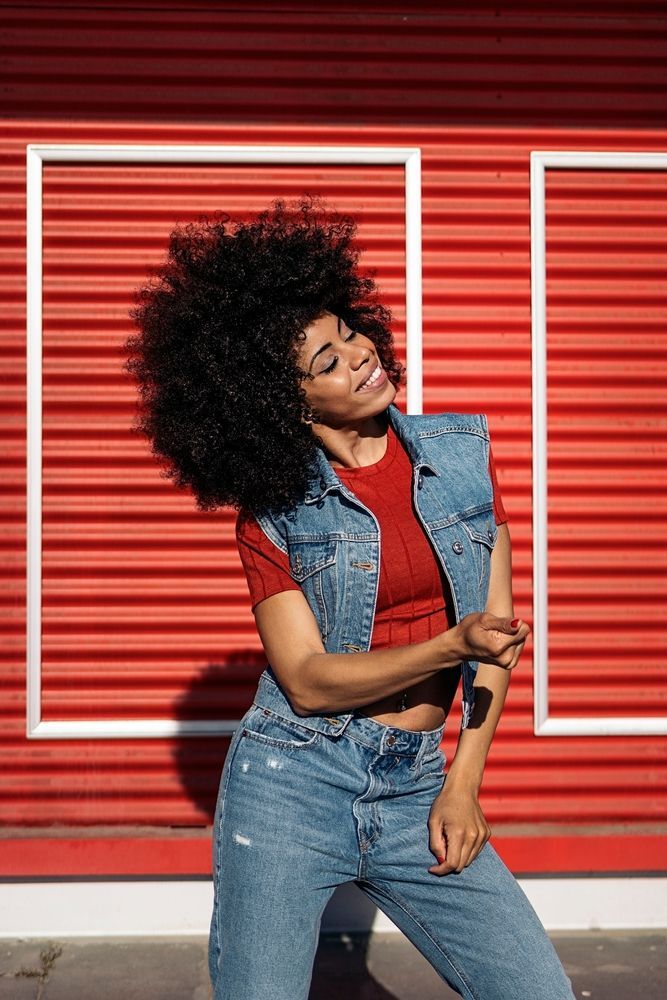 Woman dancing in a denim outfit against a red shuttered wall