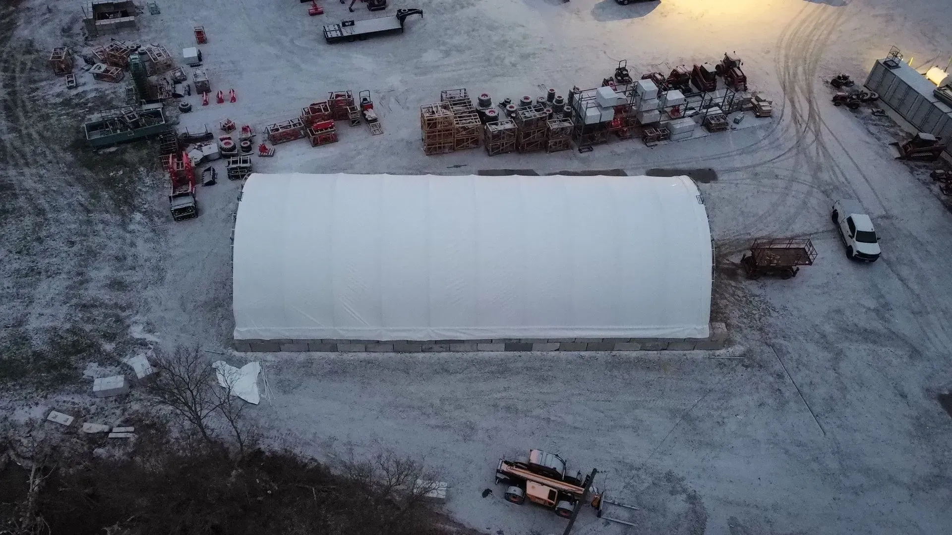 Snowy aerial view of a white warehouse with parked trucks and equipment at dusk