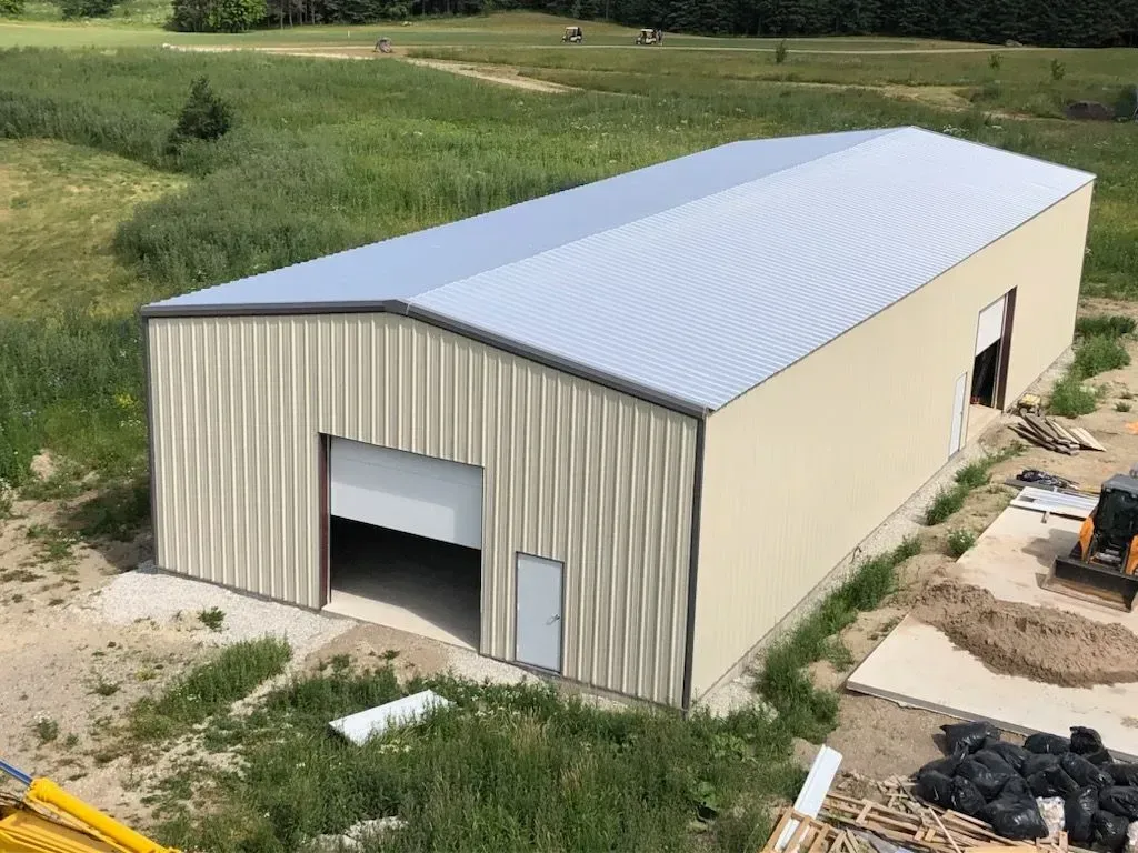 Tan metal-sided barn with a large open doorway, set in a grassy field