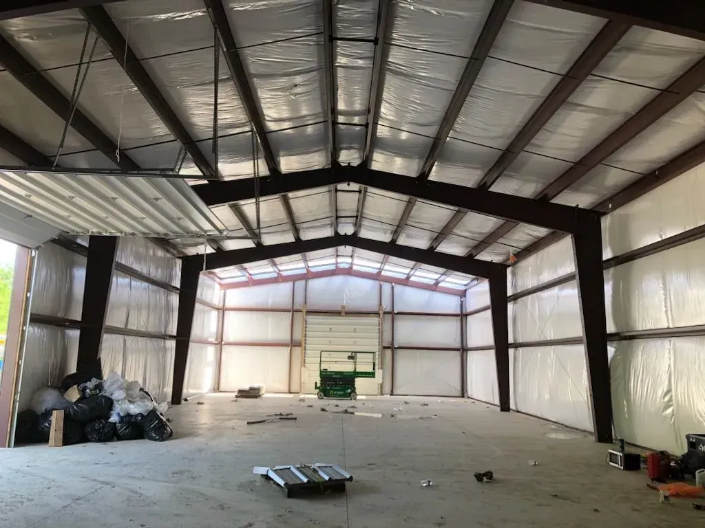 Empty warehouse interior with metal walls, exposed beams, and a small pile of debris on the floor