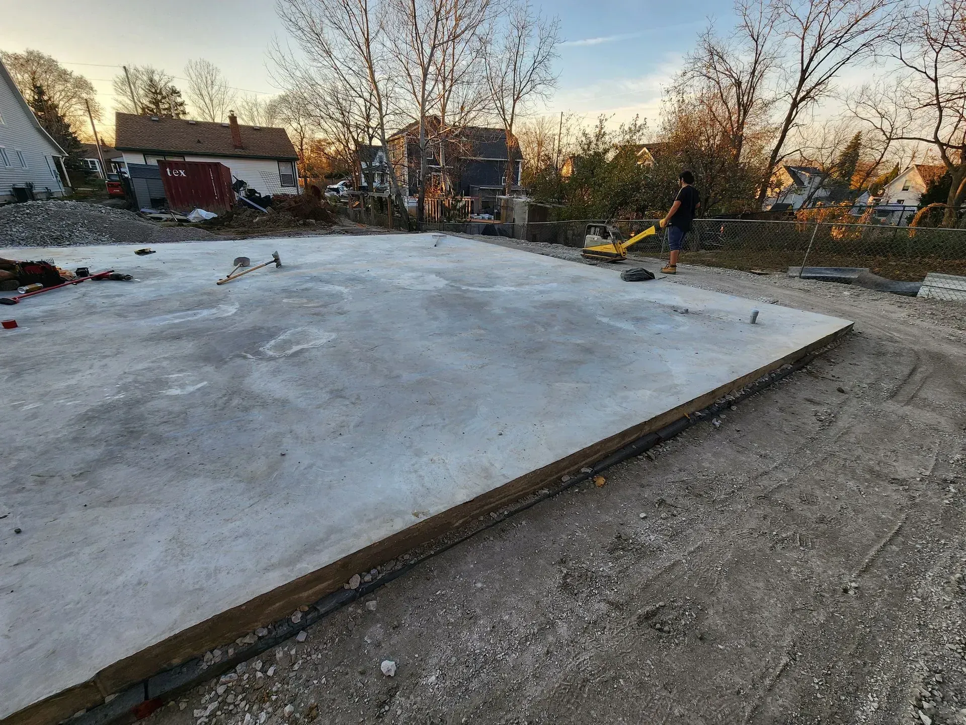 Fresh concrete slab at a construction site with trees and houses in the background at sunset