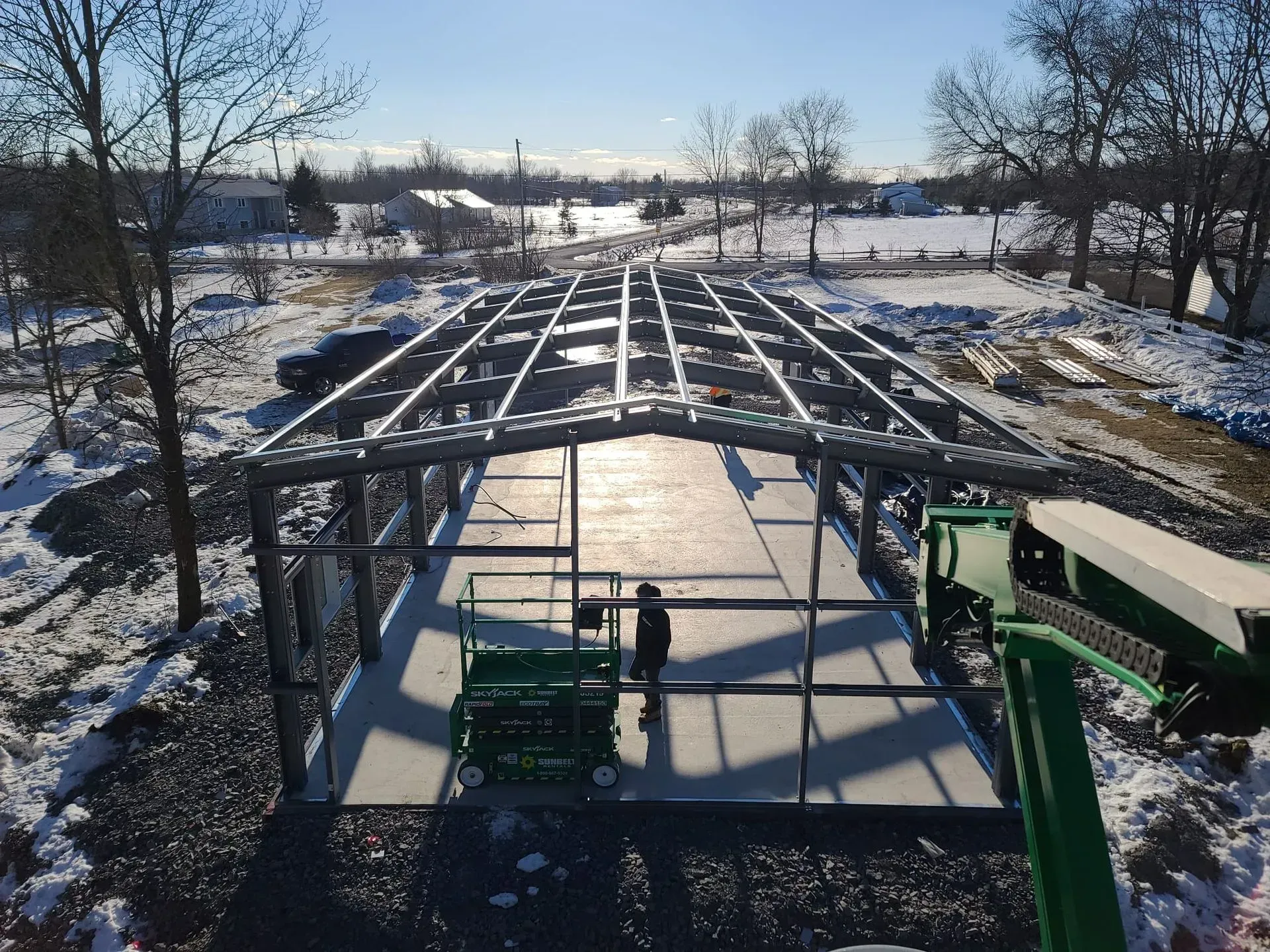 Snowy construction site with steel roof frame and two cranes, seen from above