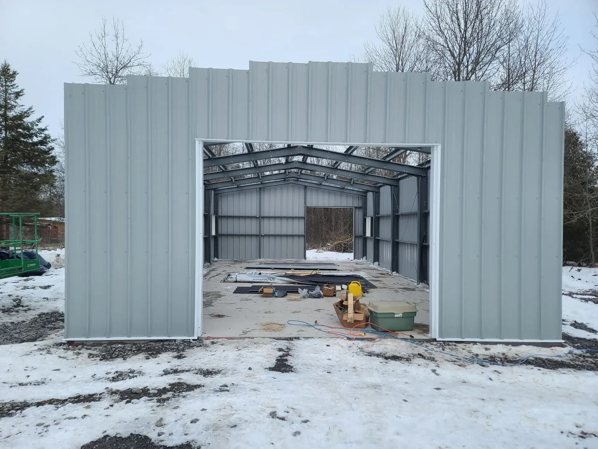 Partially built metal garage in snowy yard, with open front and construction materials inside