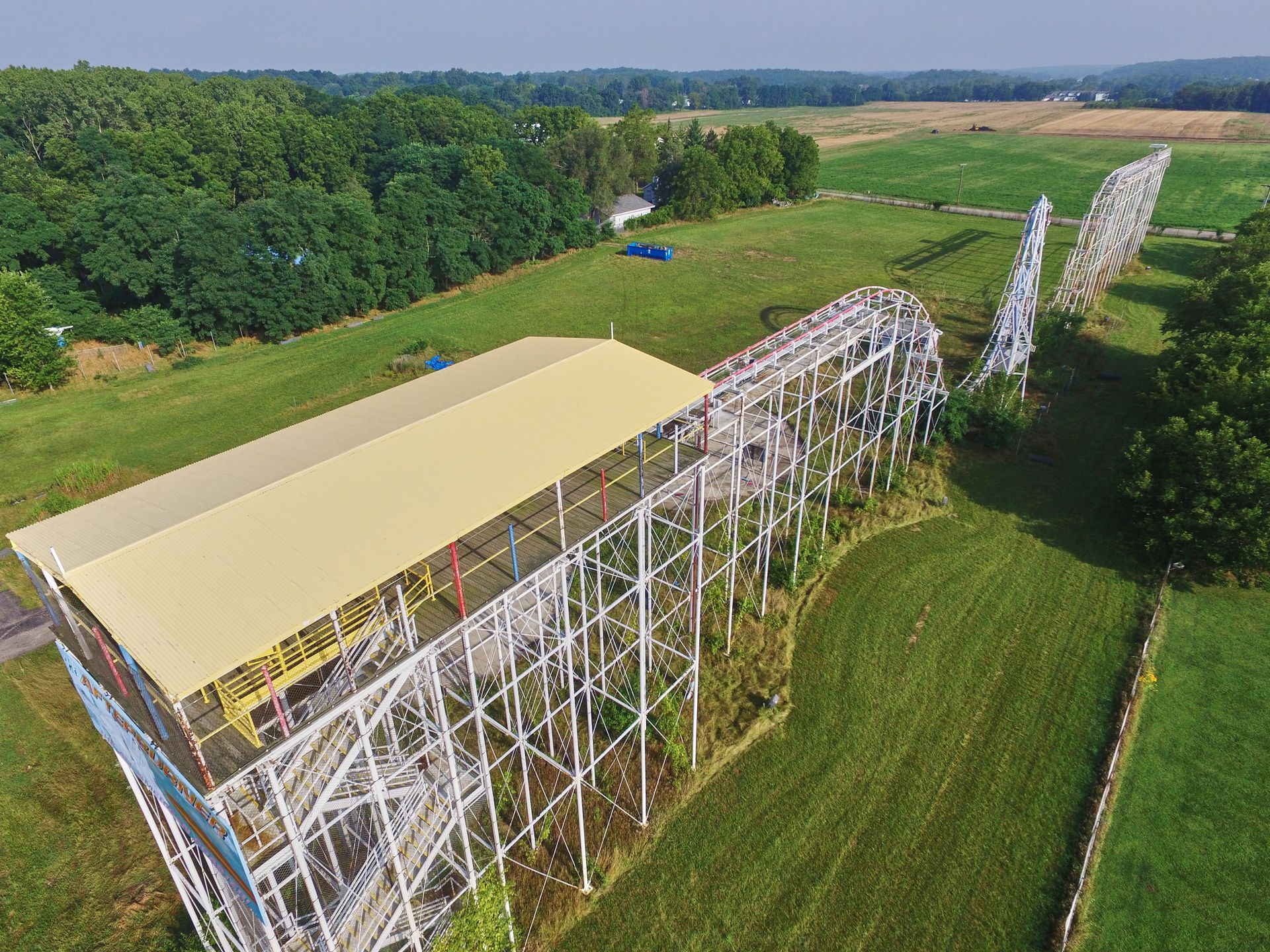 Aerial view of a roller coaster under construction beside green fields and trees