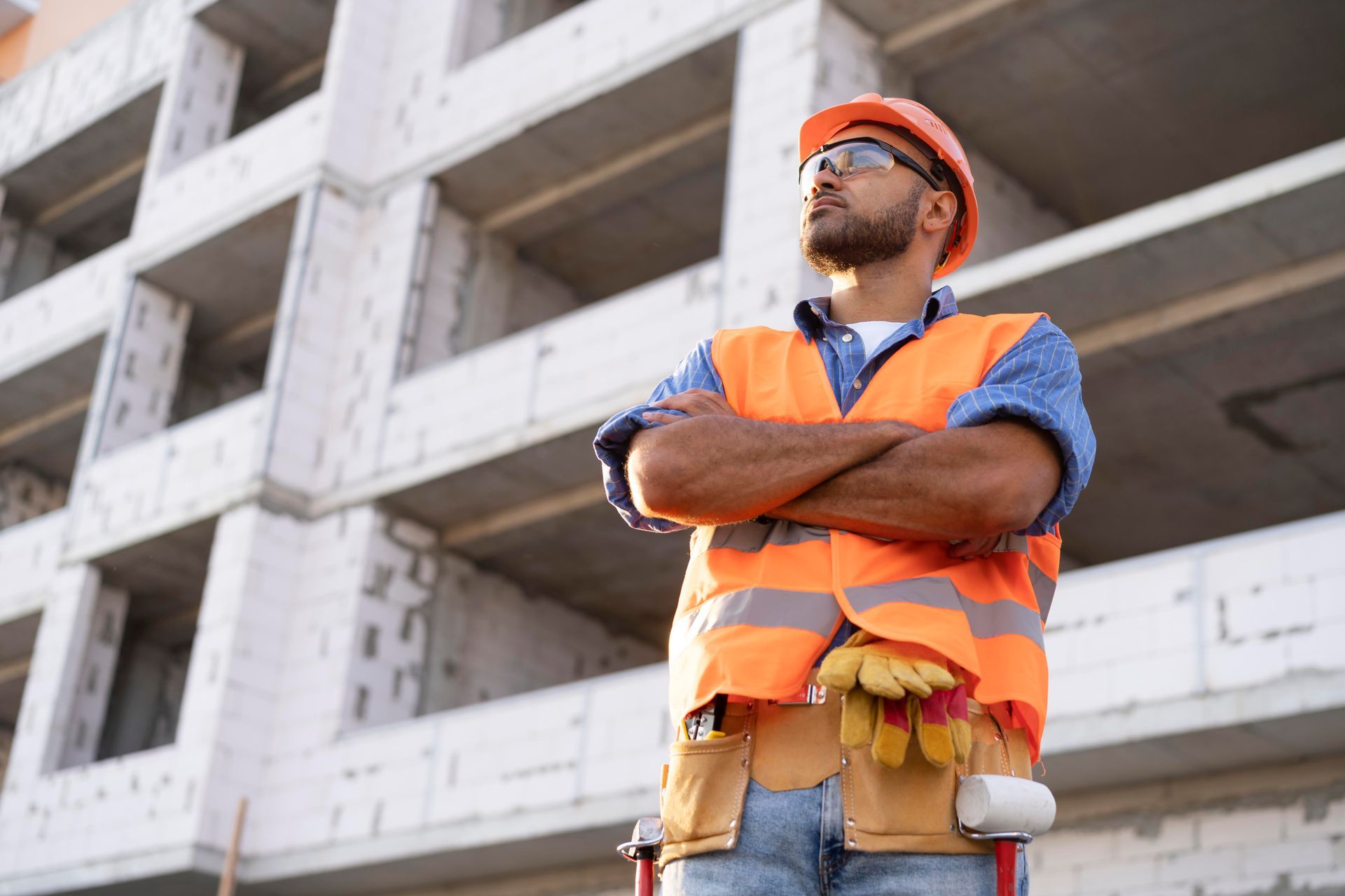 Construction worker in orange safety vest and hard hat standing arms crossed at a building site