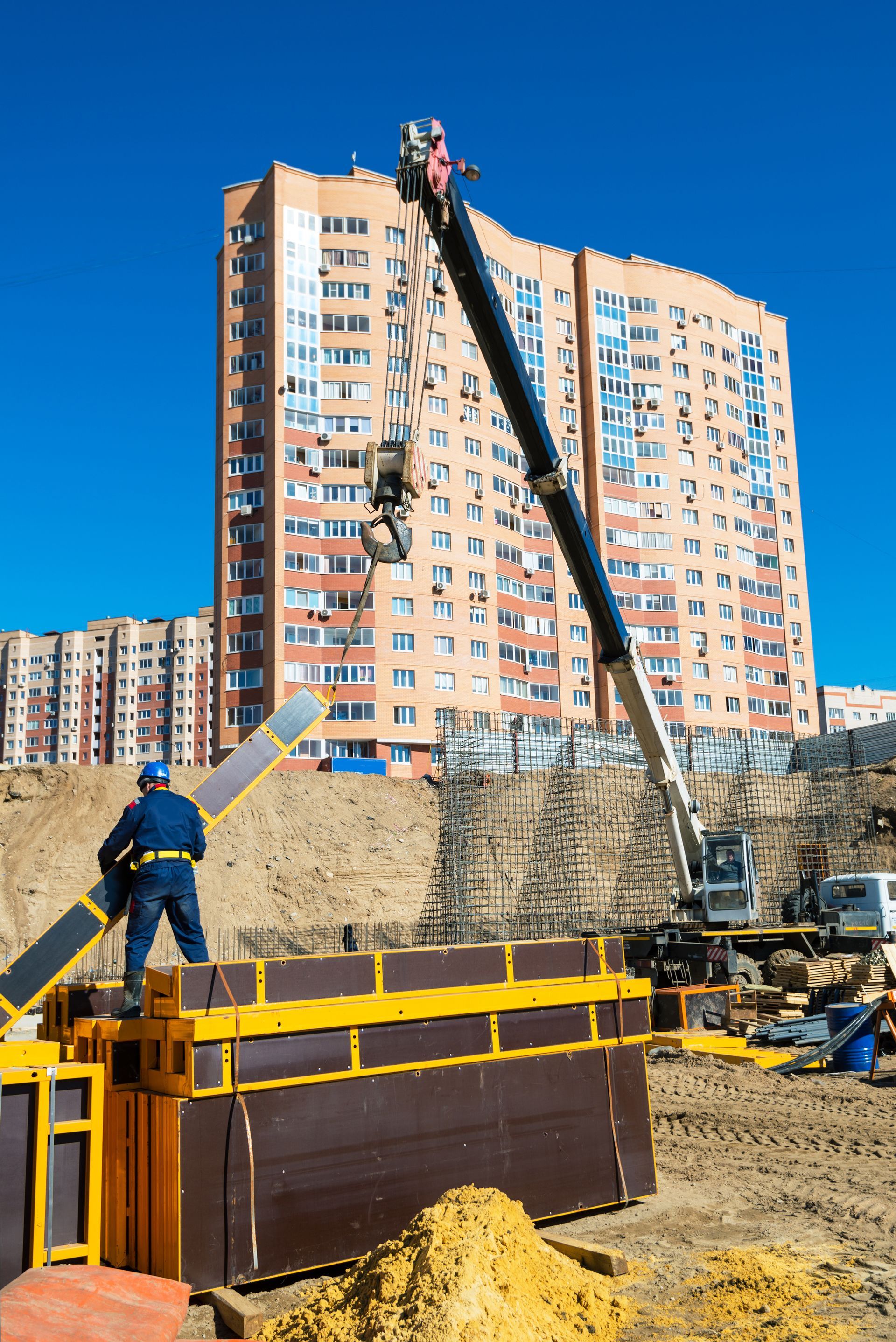 Construction crew lifting debris beside a high-rise apartment building on a muddy site