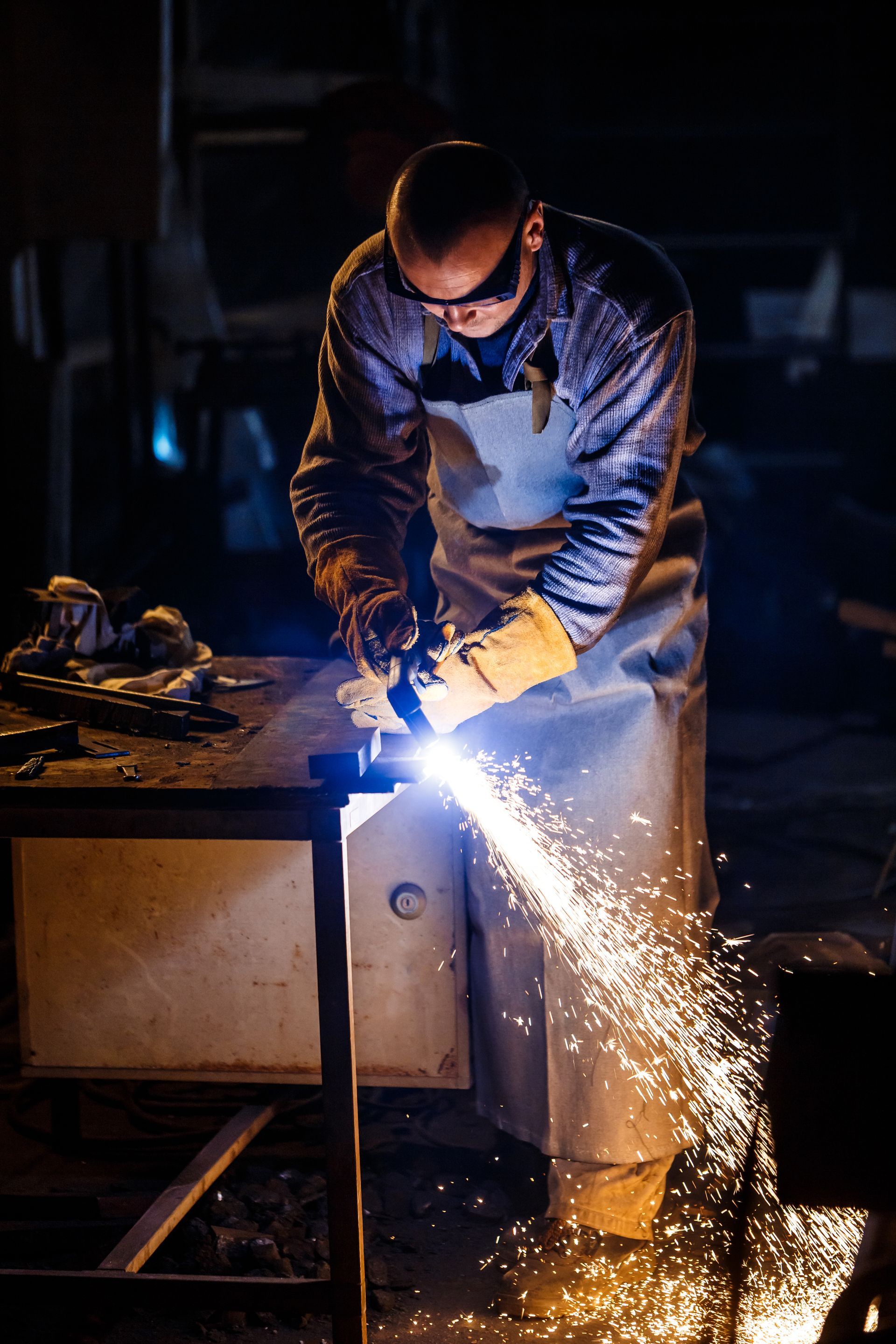 Welder in protective gear sparks metal in a dark workshop