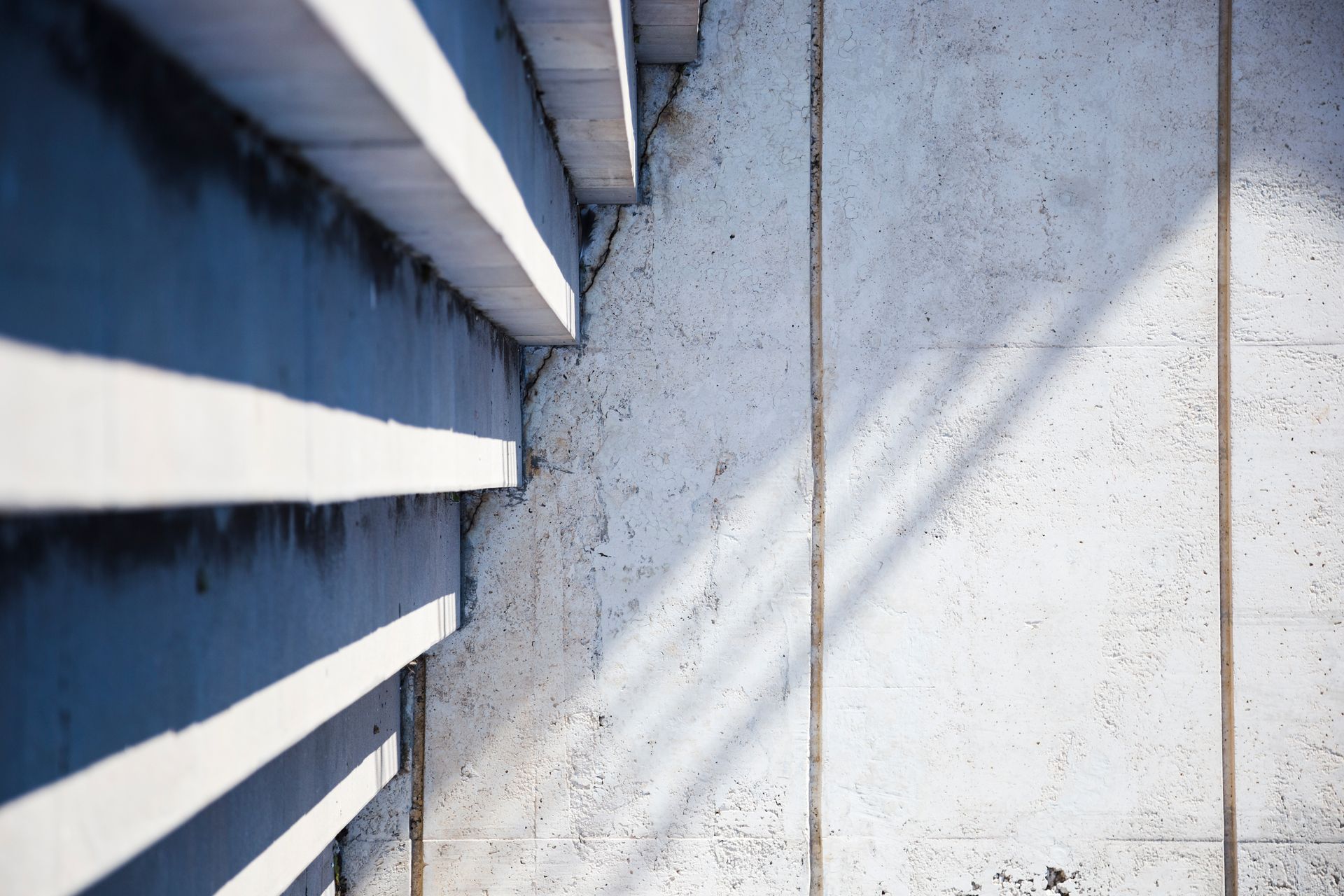 Shadows cast across white siding and a light gray wall in bright sunlight