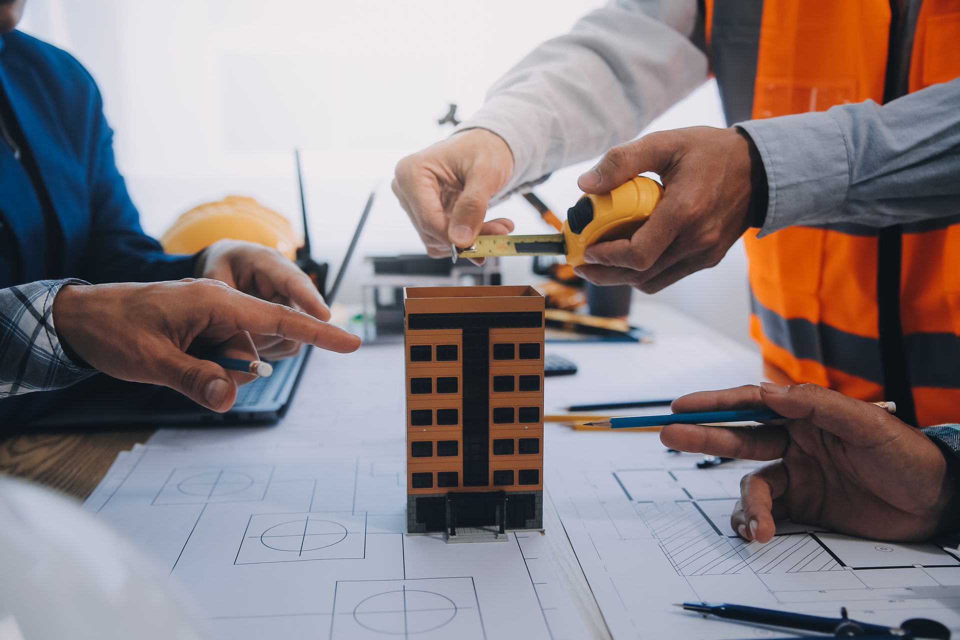 Hands around a building model on blueprints during an architecture planning meeting