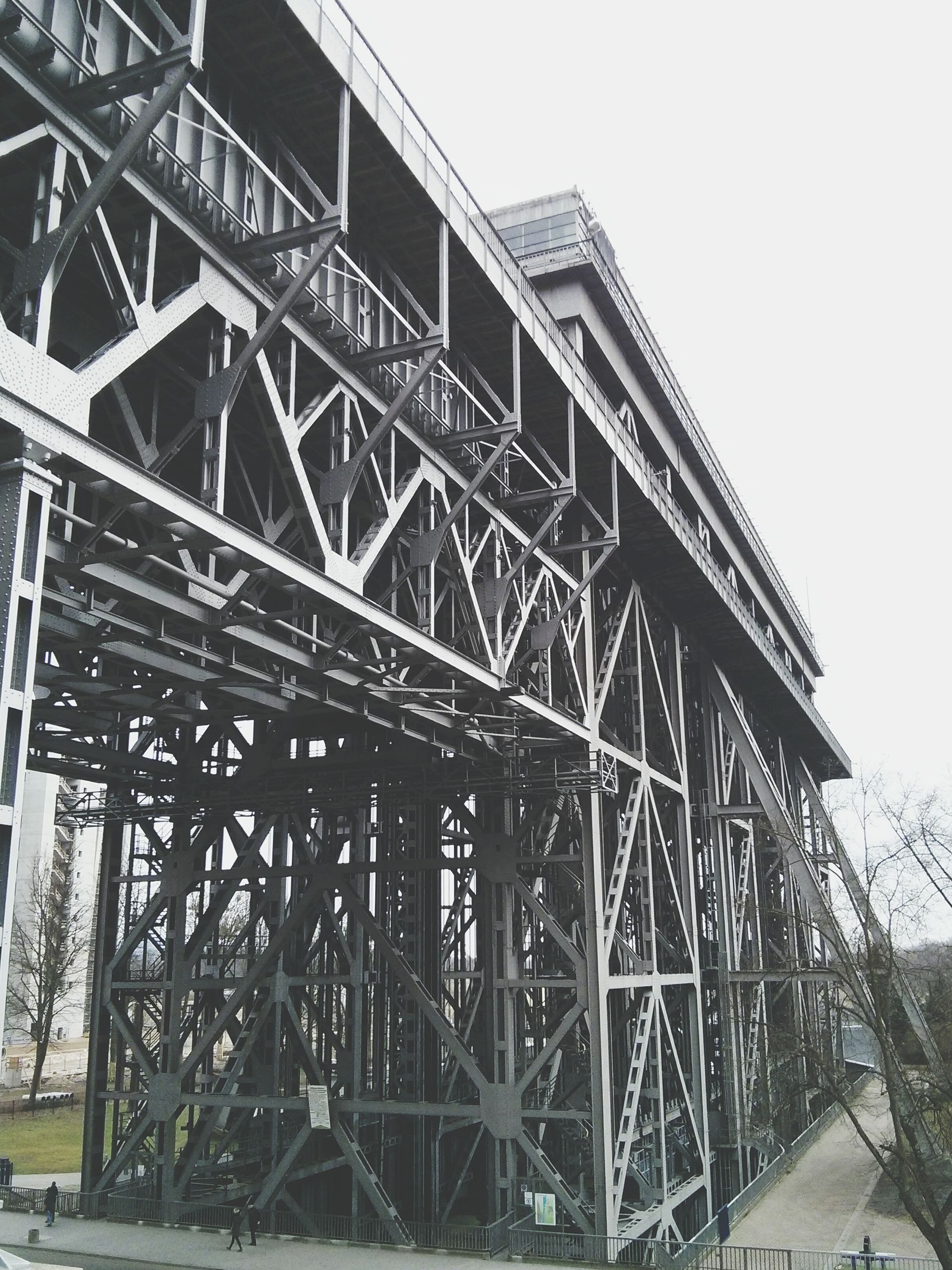 Large metal bridge support structure with steel beams and trusses beside a road, viewed from below