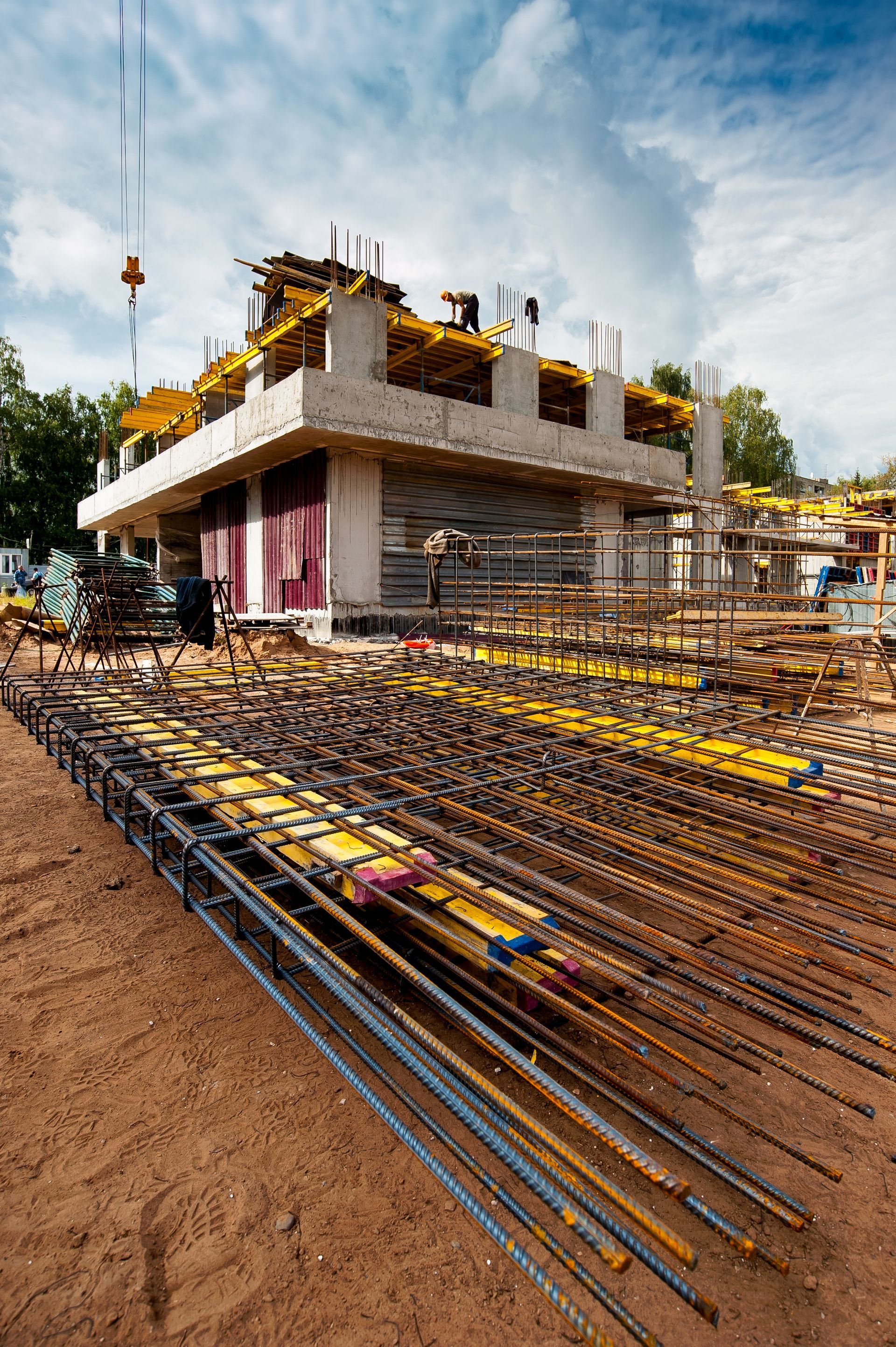 Partially built concrete house with exposed rebar and construction materials on a muddy site