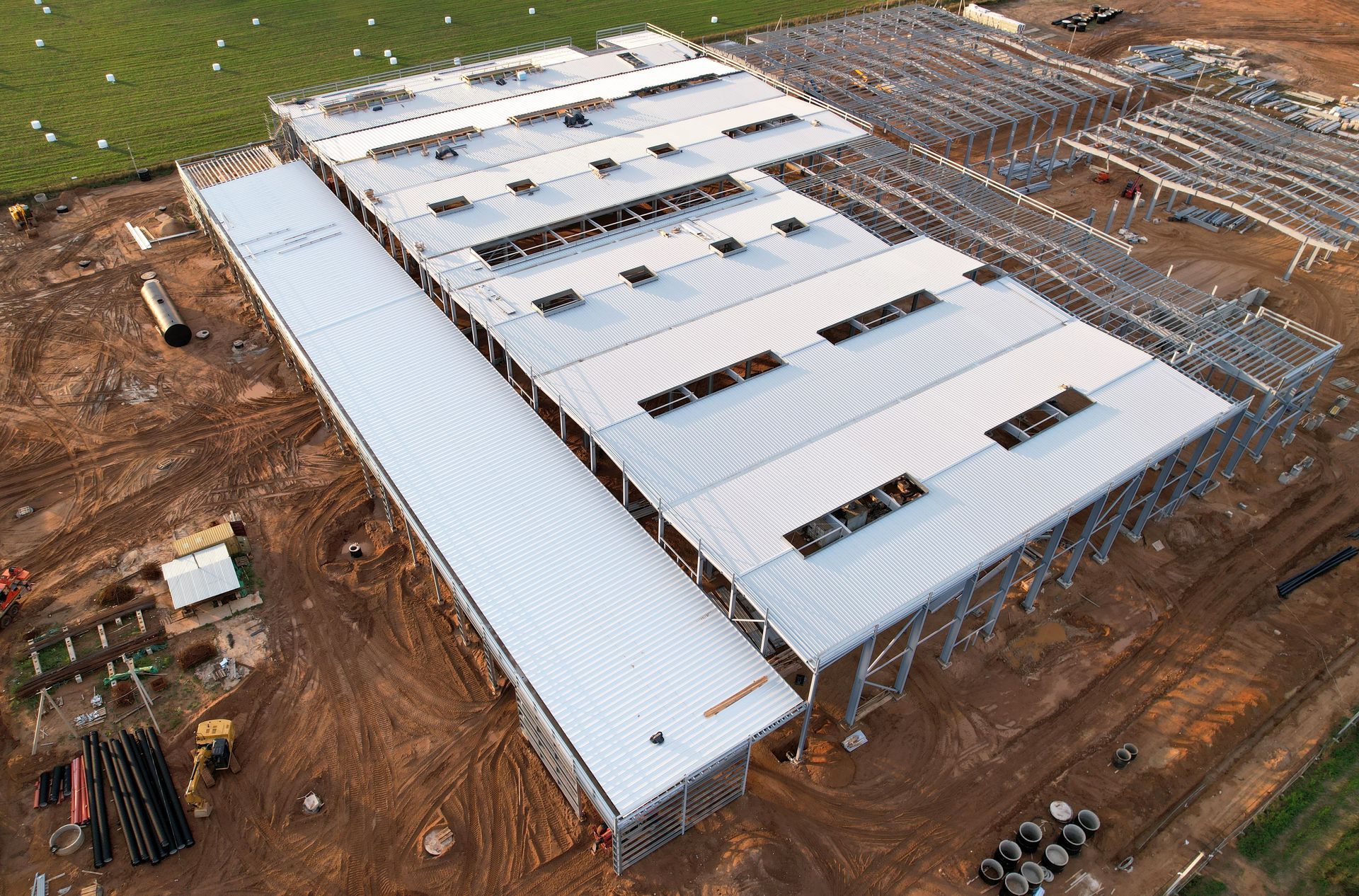 Aerial view of a large white industrial building under construction on a dirt site.