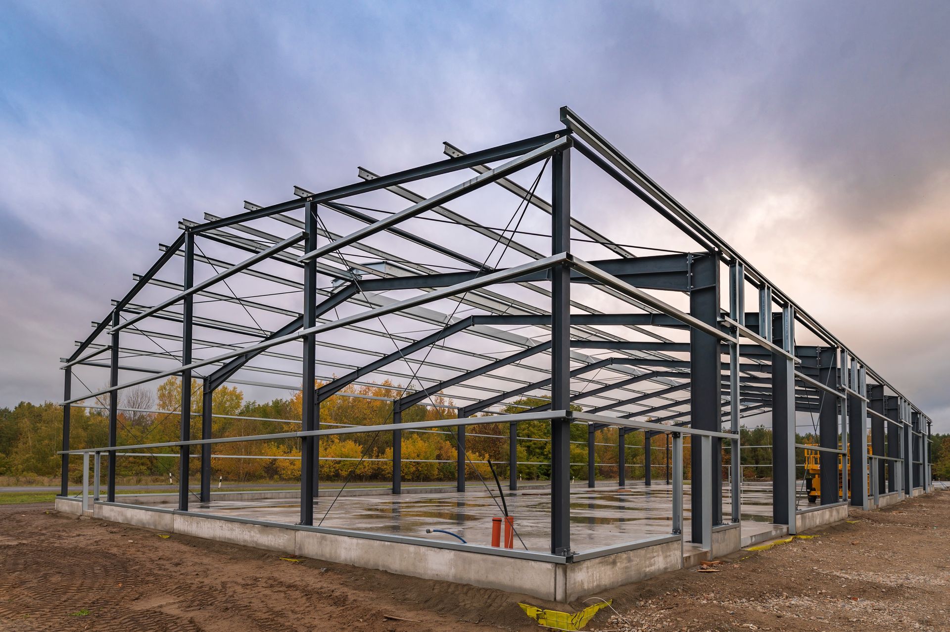 Steel warehouse frame under construction on a dirt lot at sunset.