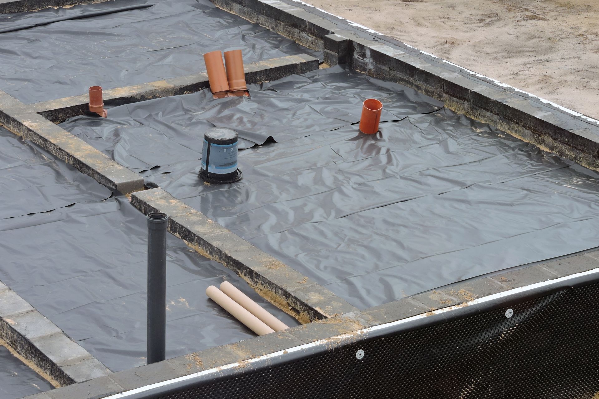 Flat roof under repair with gray waterproofing membrane and several vent pipes emerging from it
