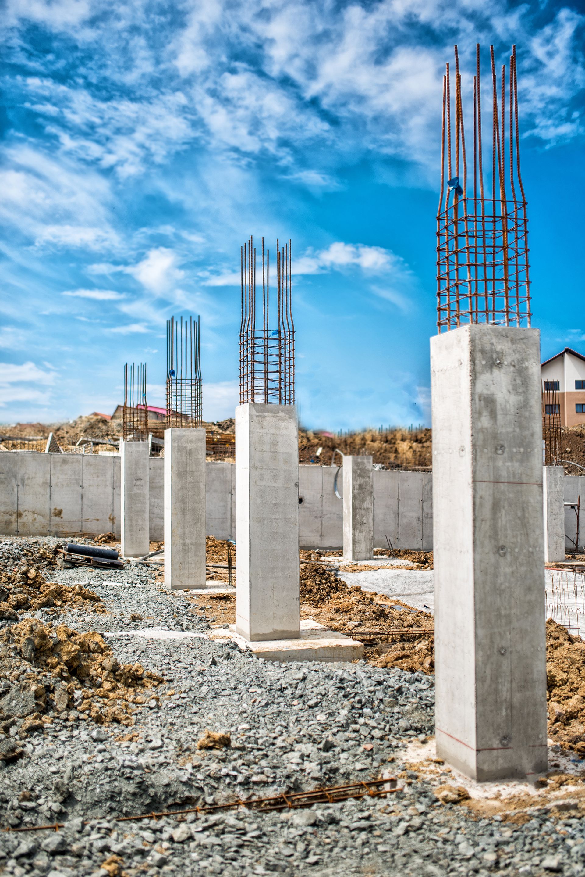 Concrete pillars with exposed rebar on a gravel construction site under a bright blue sky
