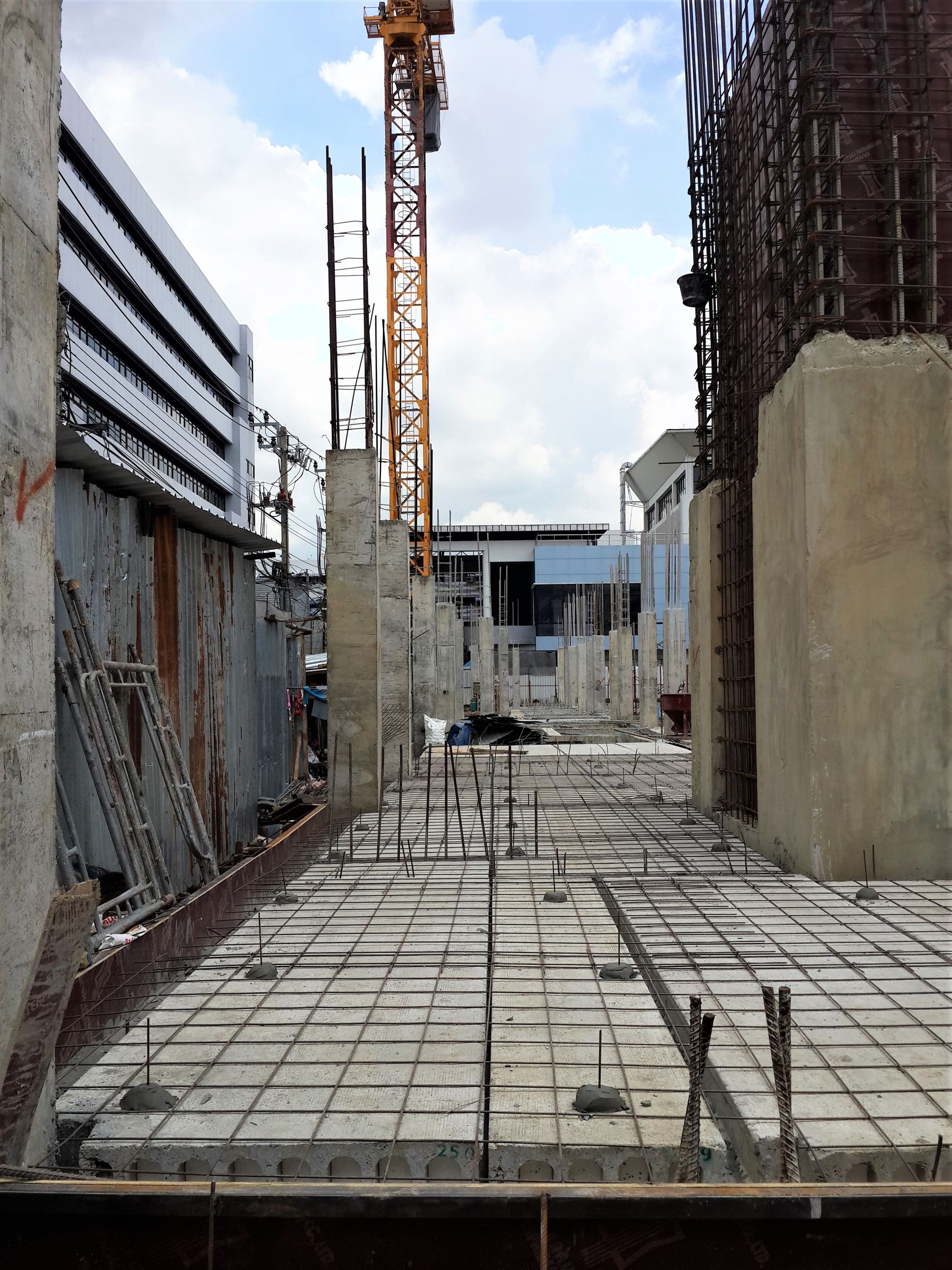 Construction site walkway with rebar grid, concrete walls, and a crane in the background