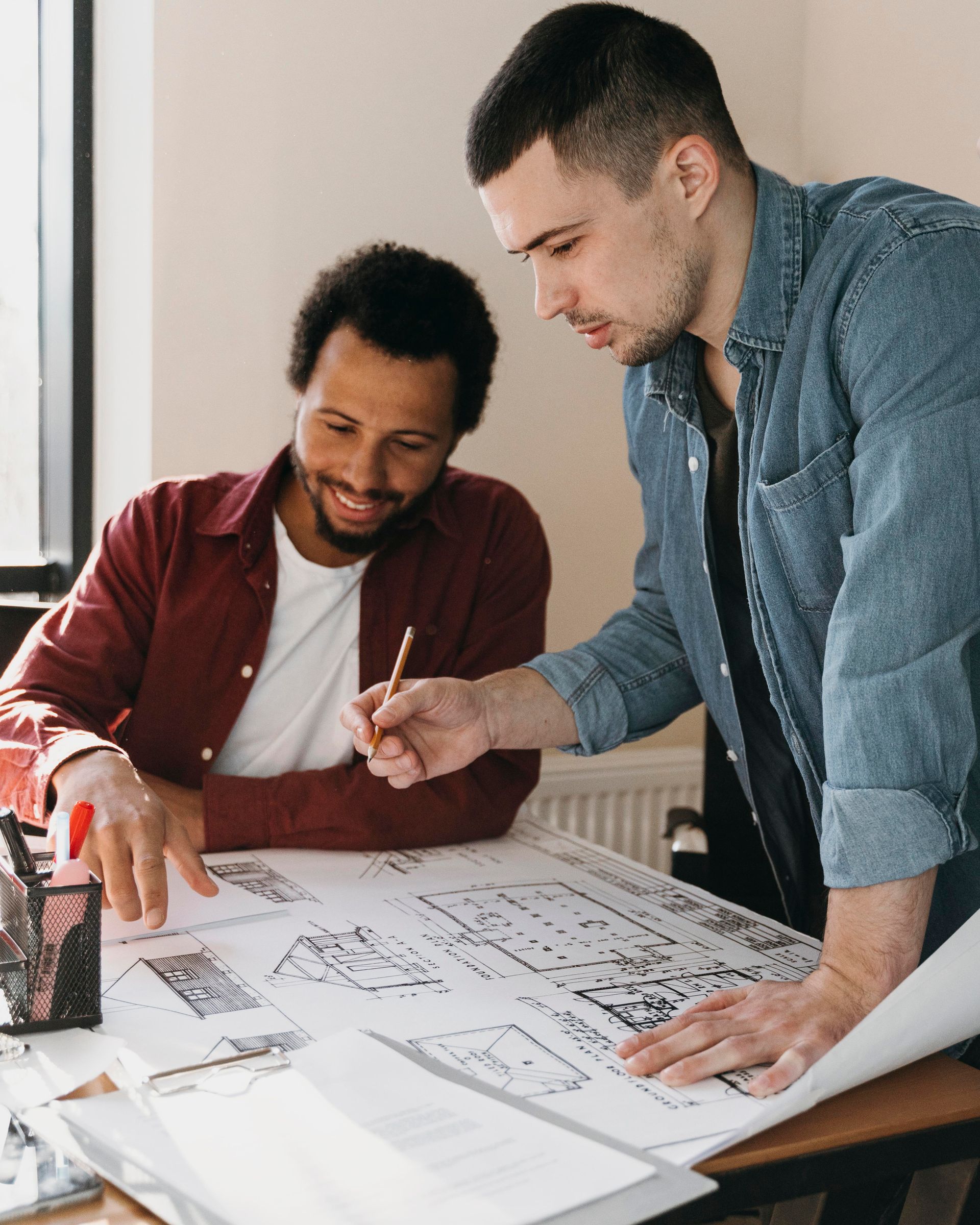 Two people reviewing a large architectural blueprint at a desk, one pointing and the other leaning in to discuss.