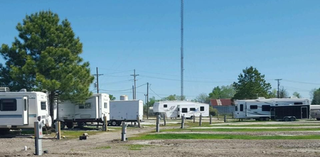 Open concrete lot beside white trailers and a warehouse under a clear blue sky