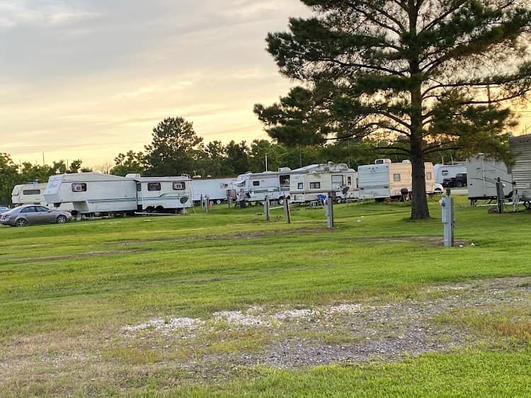 RV park with several trailers, gravel foreground, trees, and a clear blue sky