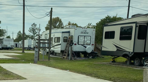 Concrete walkway in a RV park with parked trailers and utility poles under a cloudy sky