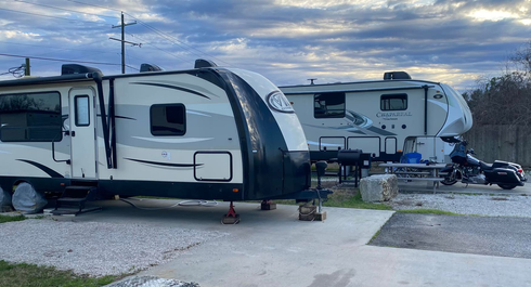 Two parked travel trailers on a paved campsite under a cloudy sky, with a light dusting of snow.