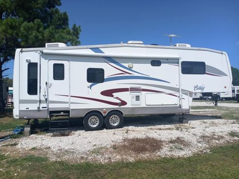 White fifth-wheel camper trailer parked on grass under a cloudy sky.