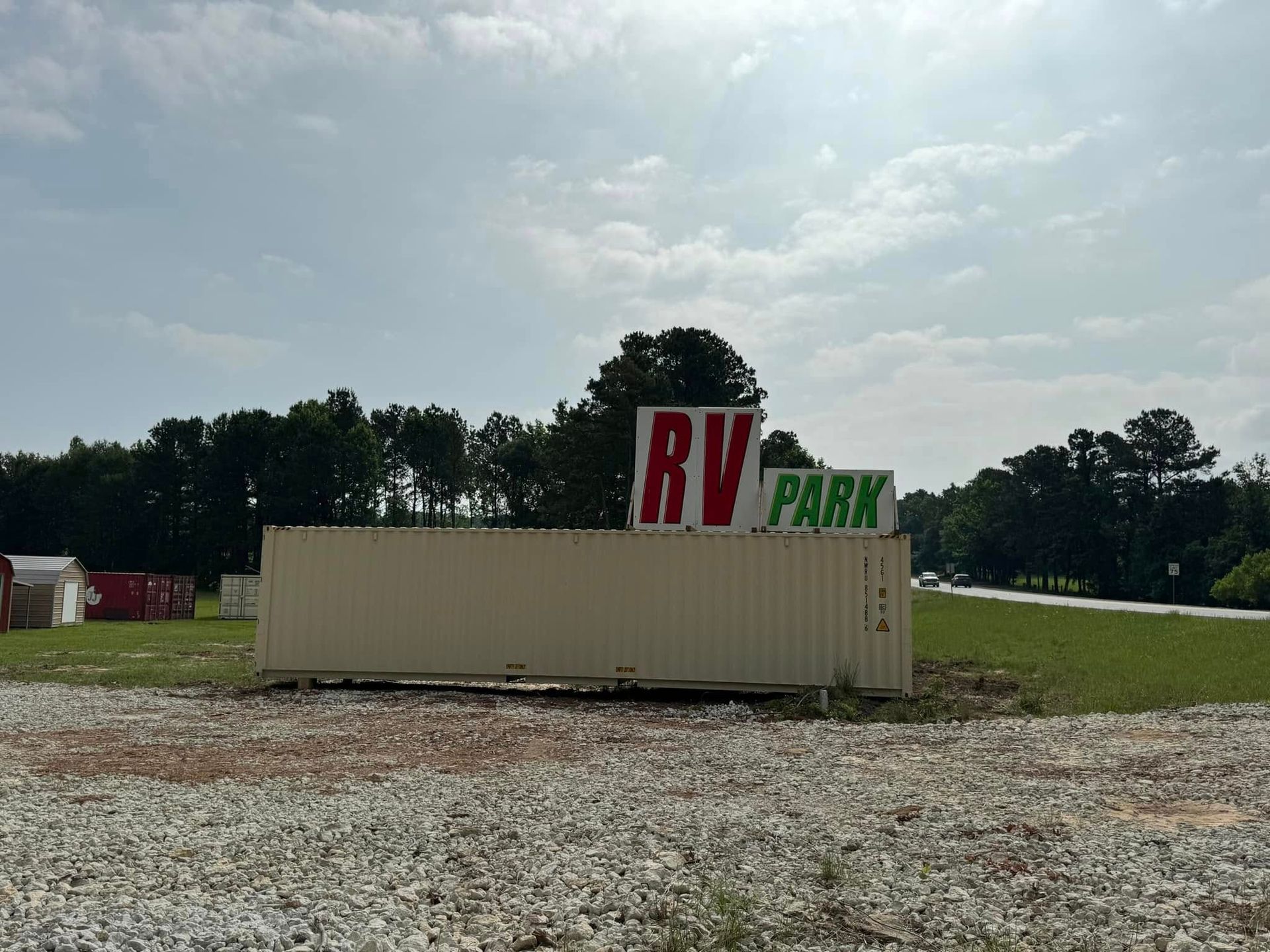 RV park sign beside trees and a road under a cloudy sky