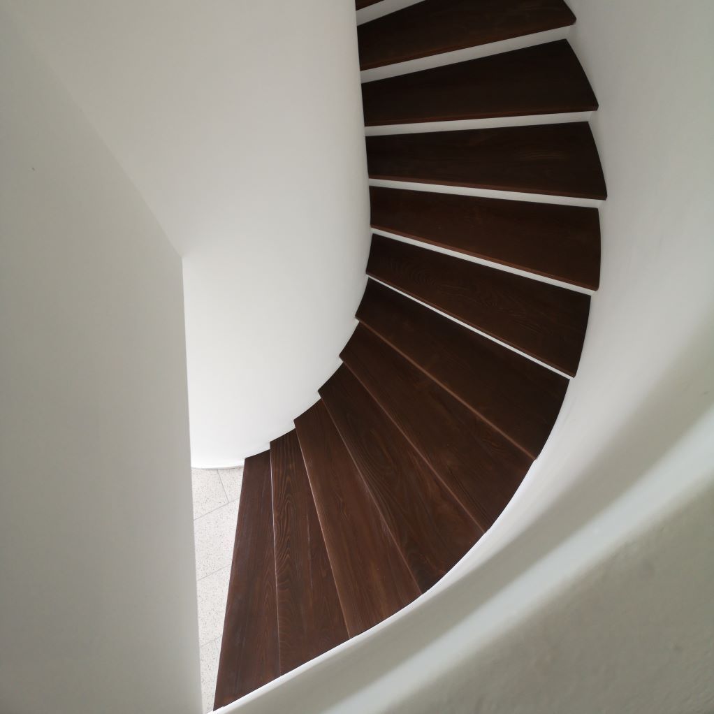 Un escalier en colimaçon avec des marches en bois et un mur blanc