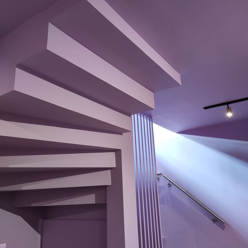 Un escalier avec des murs violets et une lumière qui brille à travers le plafond
