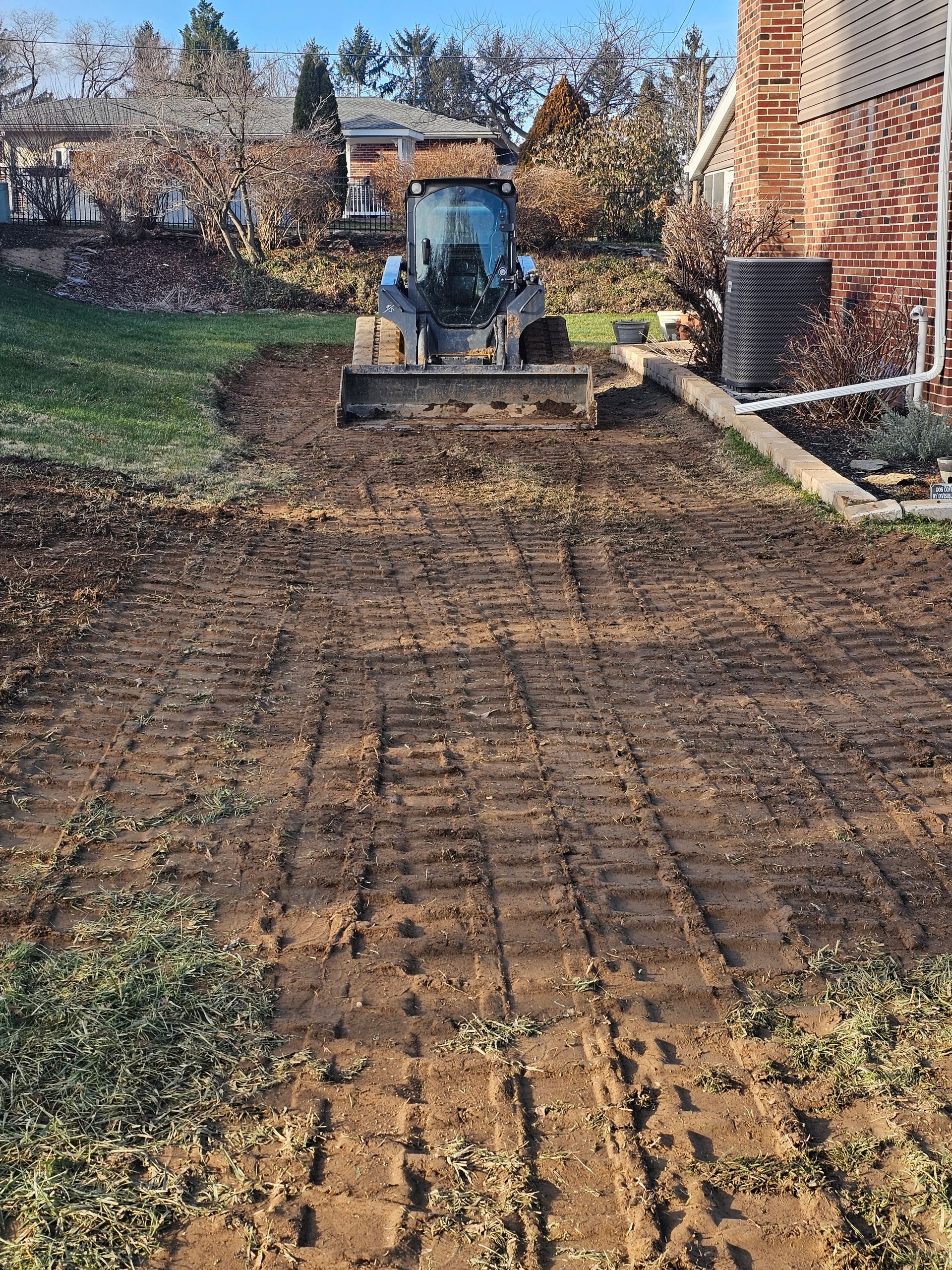 Small bulldozer on muddy ground preparing a backyard area. Brown dirt with tire tracks.