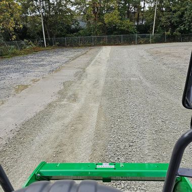 A view from a machine, grading a gravel driveway with trees in the background.