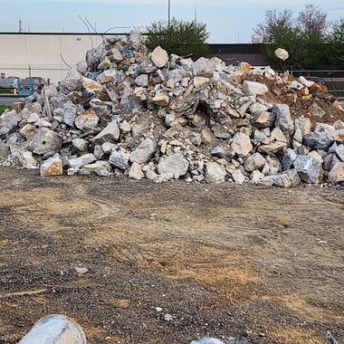 Pile of gray and tan rubble on a gravel lot near a building.