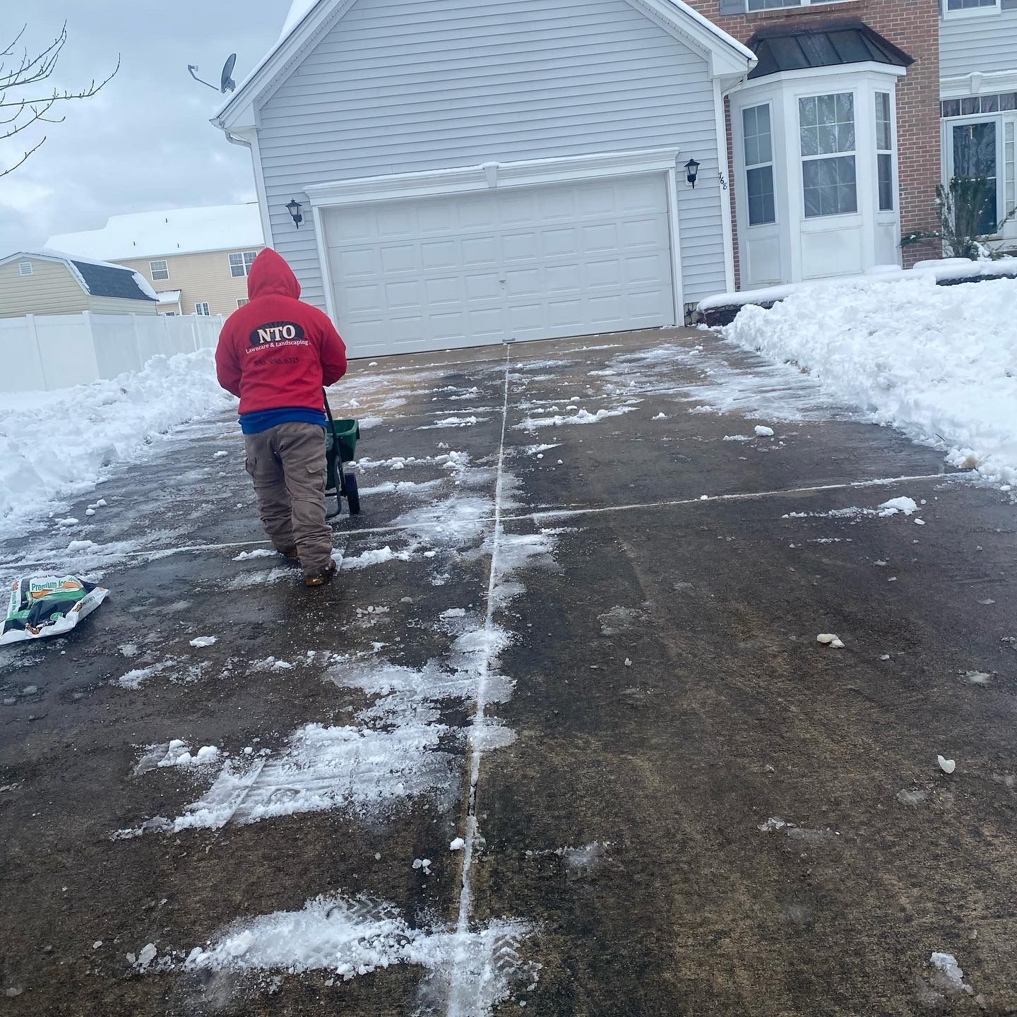 Nto lawn care & landscaping employee in red jacket shoveling snow from driveway in front of a house