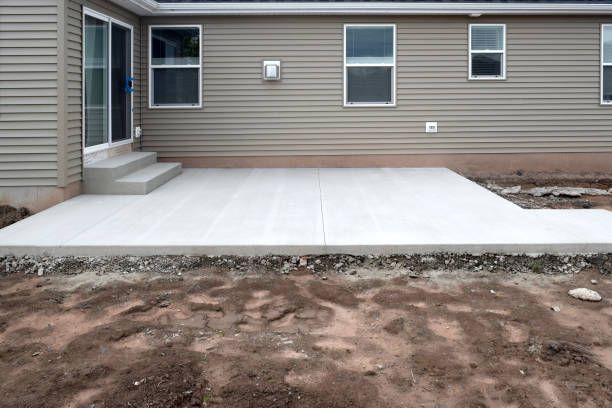New concrete patio installed by nto lawn care & landscaping in vineland with steps leading to sliding door, tan siding, and exposed dirt