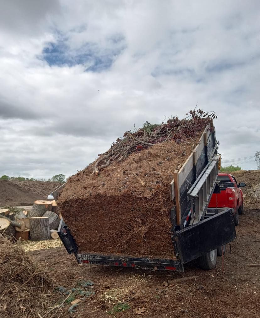 A pickup truck towing a trailer overflowing with wood chips under a cloudy sky