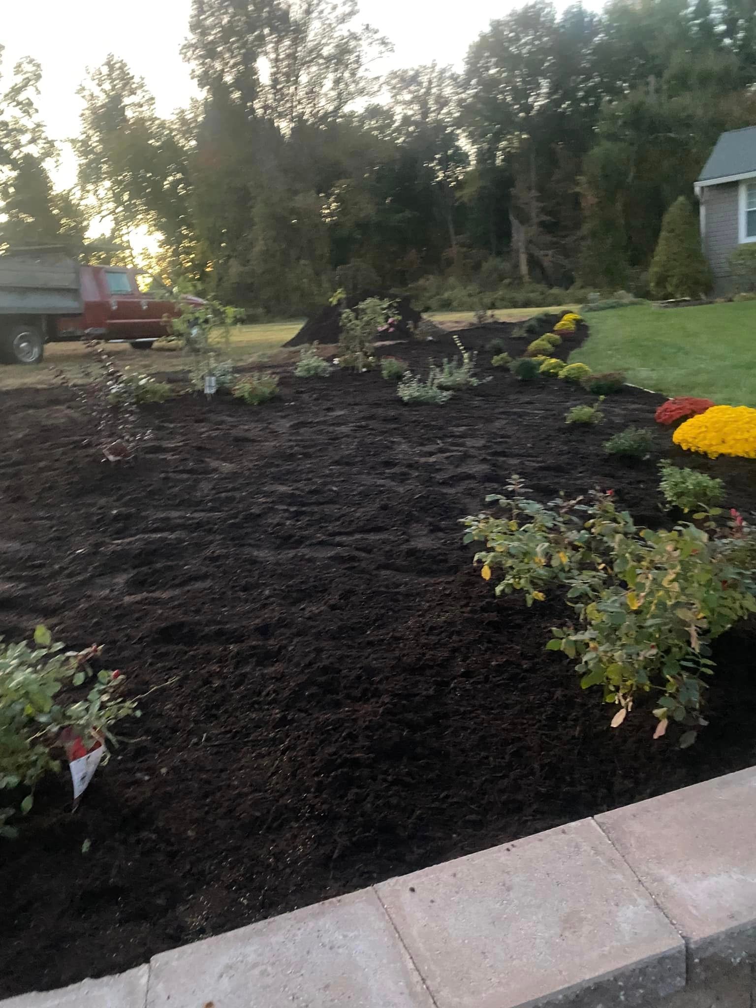Newly mulched garden bed with various plants and colorful flowers, in front of a house