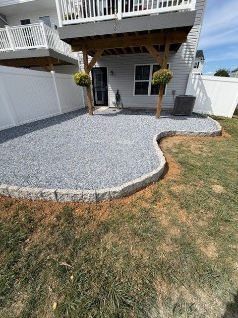 Backyard patio with gray gravel, stone edging, and a covered deck with two hanging plants