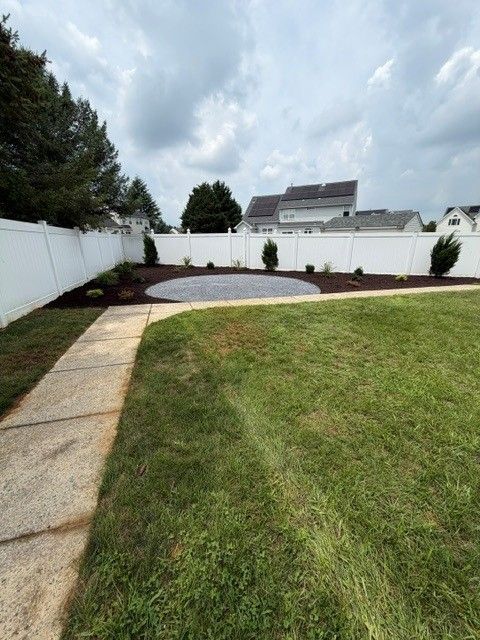 Backyard with a curved stone patio, grass lawn, white vinyl fence, and cloudy sky
