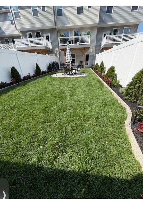 Backyard with green lawn, white fence, and townhouse patio area at the far end