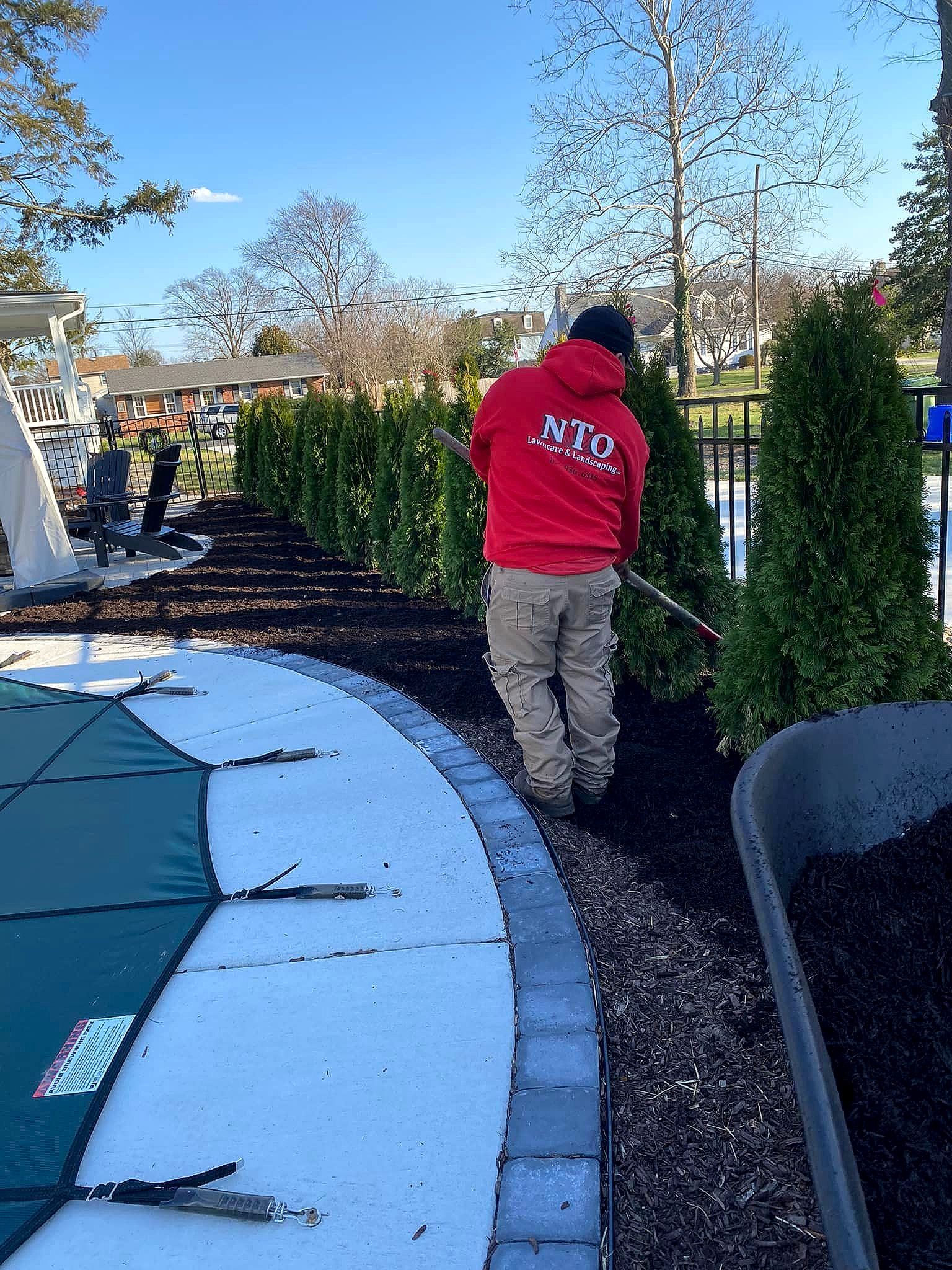 nto lawn care & landscaping employee in red hoodie raking mulch in a landscaped area next to a pool