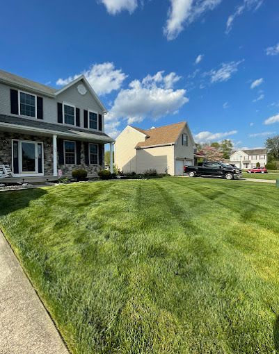Suburban homes with a well-manicured green lawn under a bright blue sky with clouds