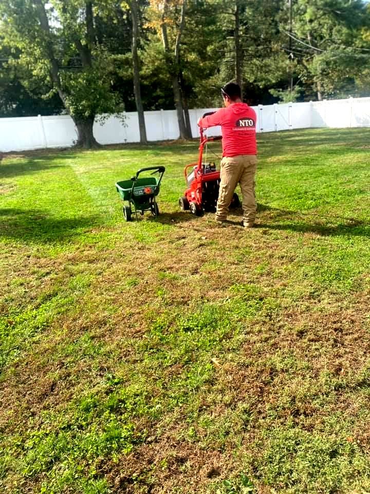 nto lawncare & landscaping employee aerating a lawn with machine, fertilizer spreader nearby