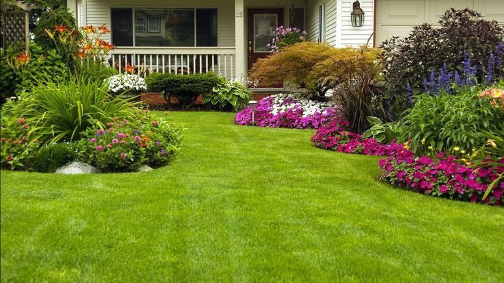 Green lawn and vibrant flowerbeds border a house with a white porch