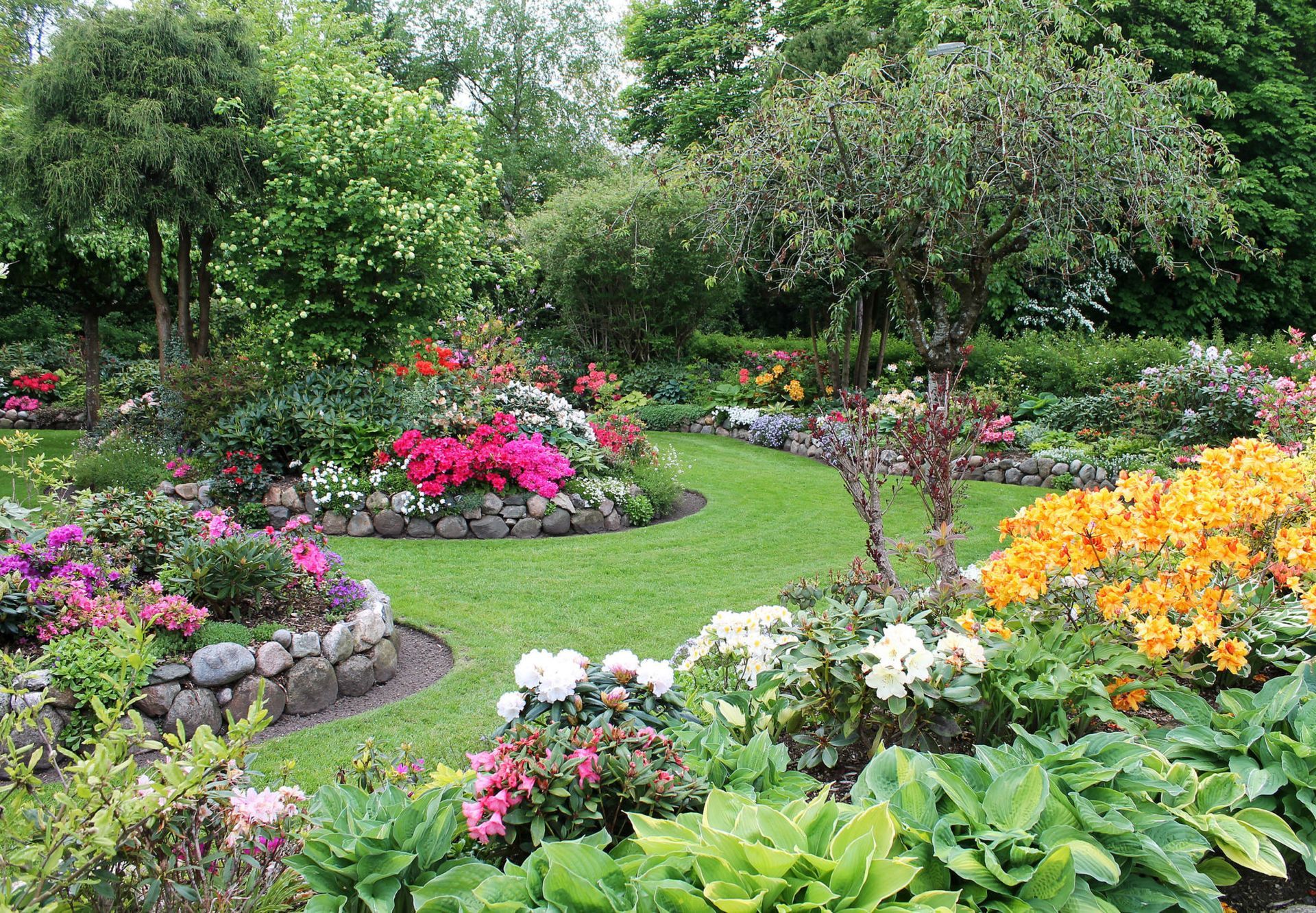 Lush garden with winding green path, bordered by rock walls and vibrant flowerbeds in various colors