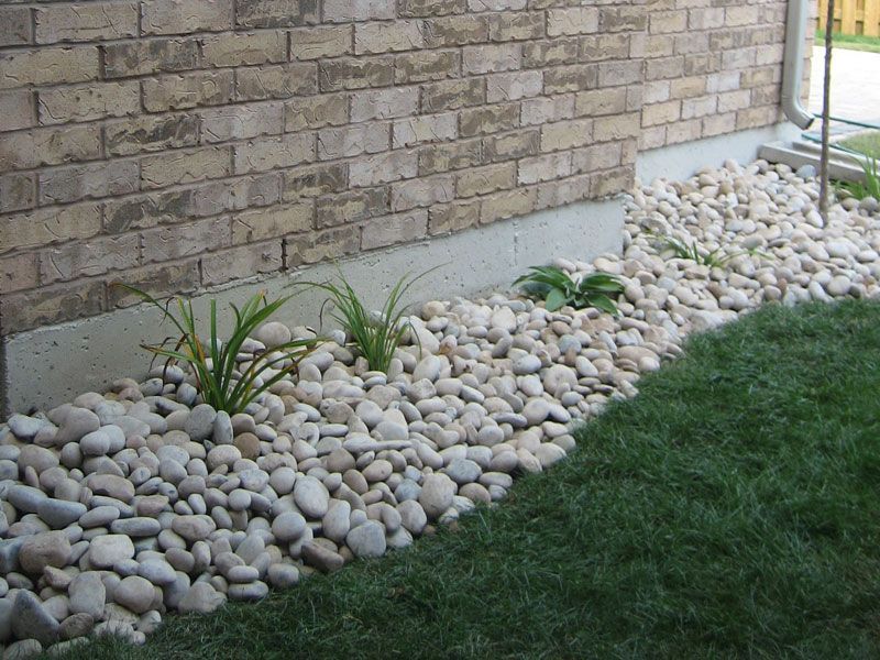 Gravel bed with small plants borders a brick wall and green lawn