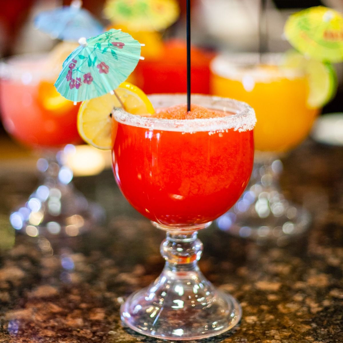 Colorful frozen cocktails in stemmed glasses, garnished with citrus and umbrellas.
