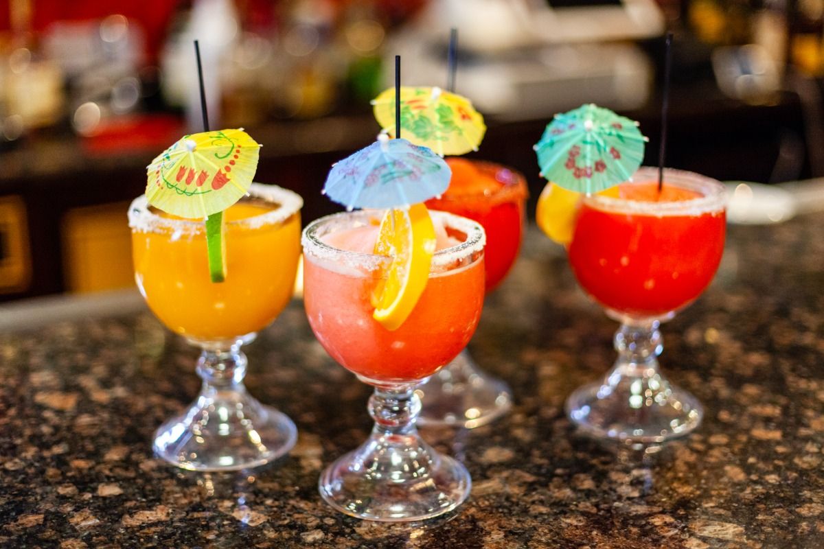 Cocktails in stemmed glasses with sugar rims, garnished with fruit and miniature umbrellas.