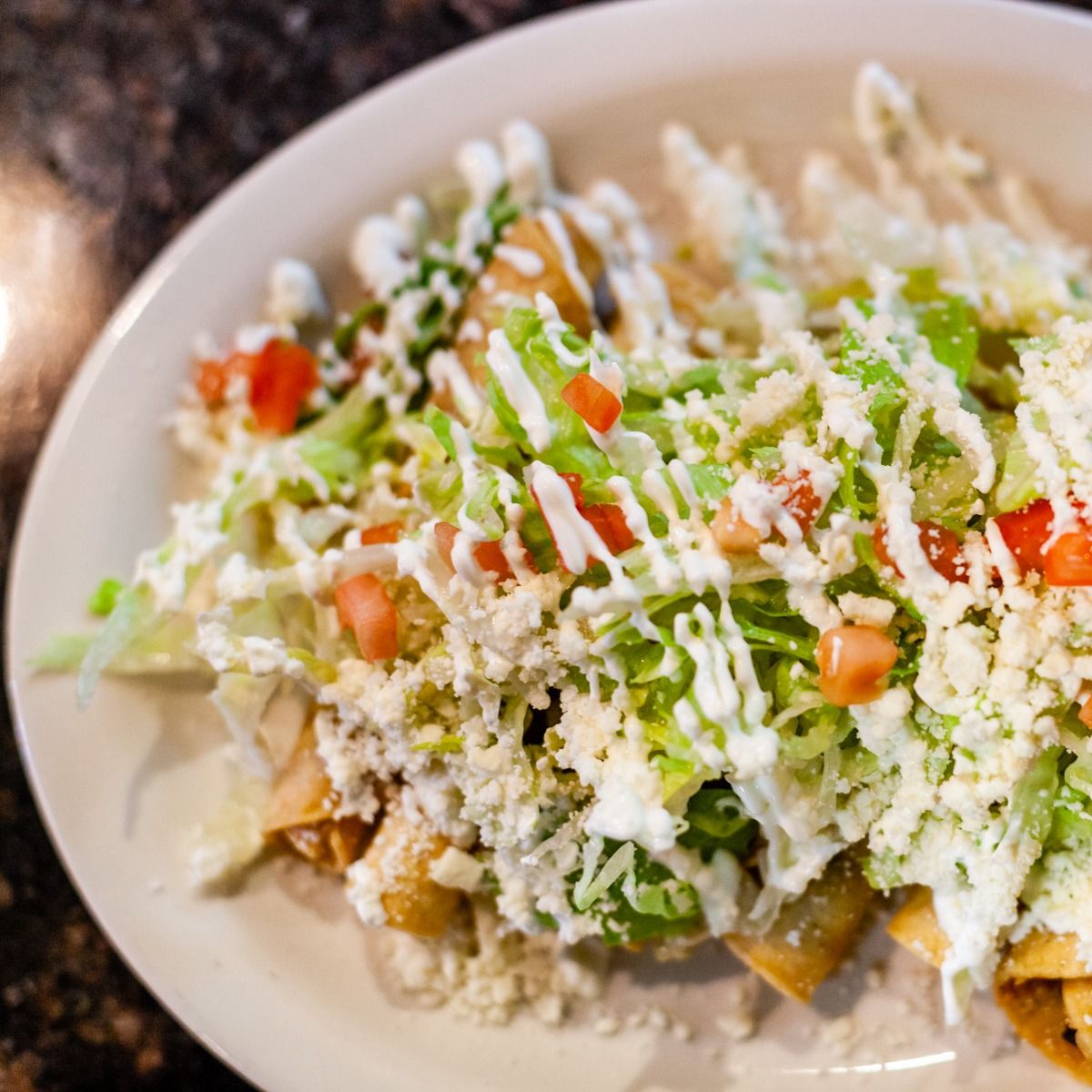 Plate of Mexican food: fried tortillas topped with lettuce, tomatoes, cheese, and crema.